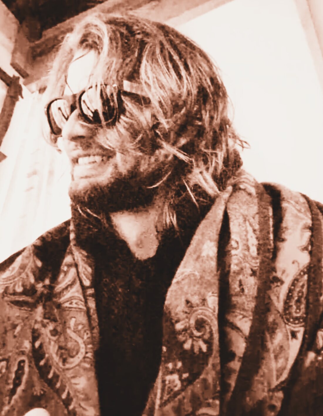 Matthias in three-quarter profile, laughing, in a patterned coat under hard window light.